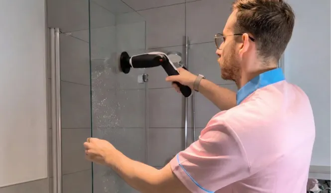 Cleaner scrubbing shower glass with a cleaning machine in a Luxembourg home